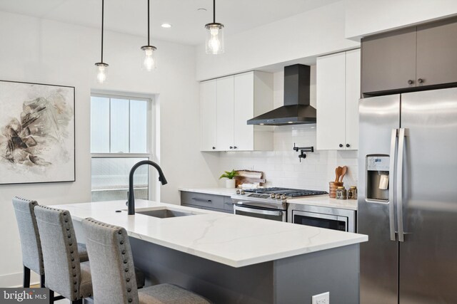 kitchen with a breakfast bar, wall chimney range hood, tasteful backsplash, a sink, and stainless steel appliances