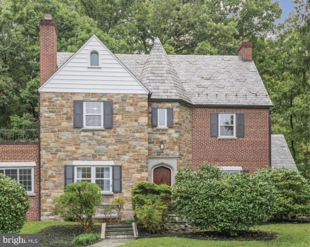 tudor-style house featuring a high end roof, a chimney, and stone siding