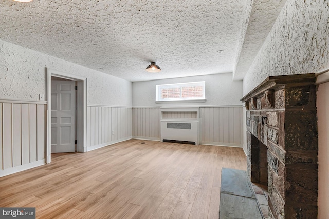 6911 Wells Pkwy, University Park, MD 20782 - unfurnished living room featuring a textured wall, wood finished floors, a fireplace, a wainscoted wall, and a textured ceiling