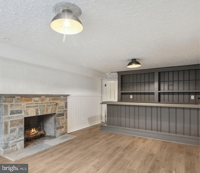unfurnished living room featuring a textured ceiling, wainscoting, wood finished floors, and a fireplace
