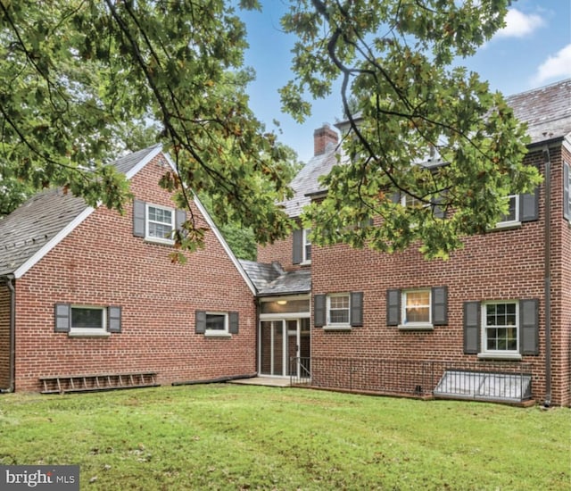back of property featuring a yard, brick siding, a chimney, and a shingled roof