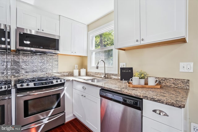 kitchen with white cabinets, stainless steel appliances, light stone counters, and a sink