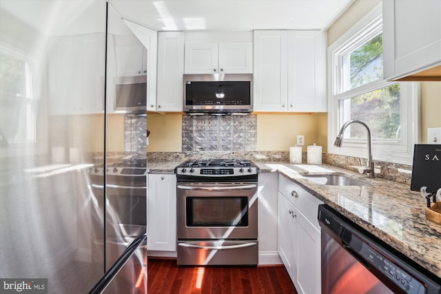 kitchen with light stone countertops, dark wood-type flooring, white cabinetry, a sink, and appliances with stainless steel finishes