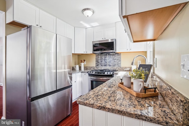 kitchen with appliances with stainless steel finishes, tasteful backsplash, light stone counters, dark wood-style floors, and white cabinetry