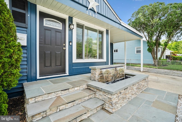 doorway to property with board and batten siding, fence, and covered porch
