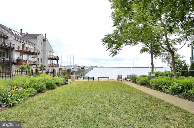 dock area featuring fence, a water view, and a yard