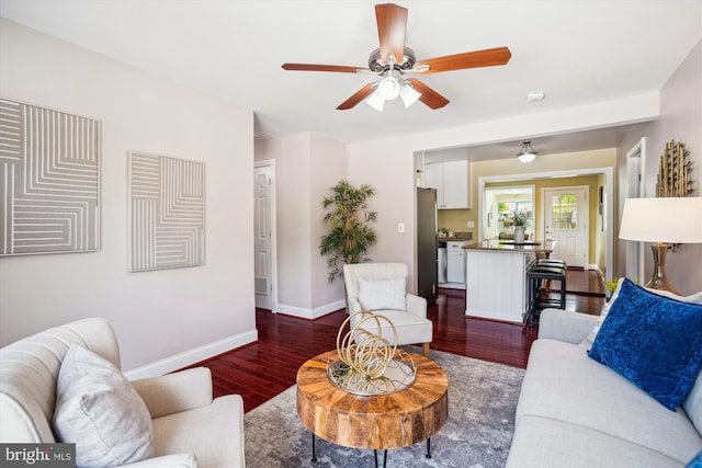 living area featuring baseboards, a ceiling fan, and dark wood-style floors