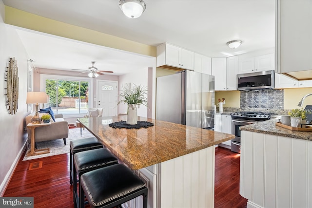 kitchen with dark wood finished floors, a center island, dark stone countertops, stainless steel appliances, and white cabinetry