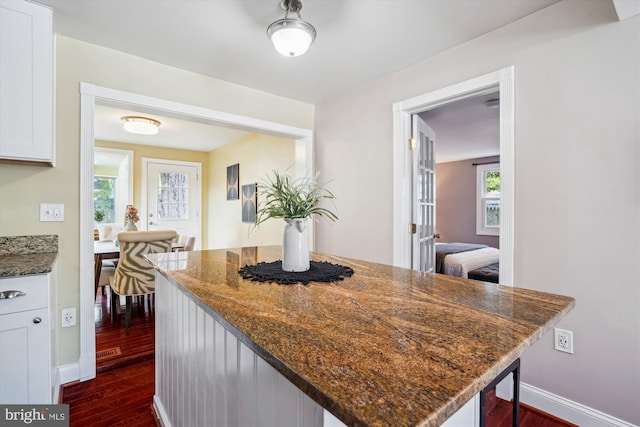 kitchen with dark wood-style flooring, a center island, baseboards, white cabinets, and dark stone countertops