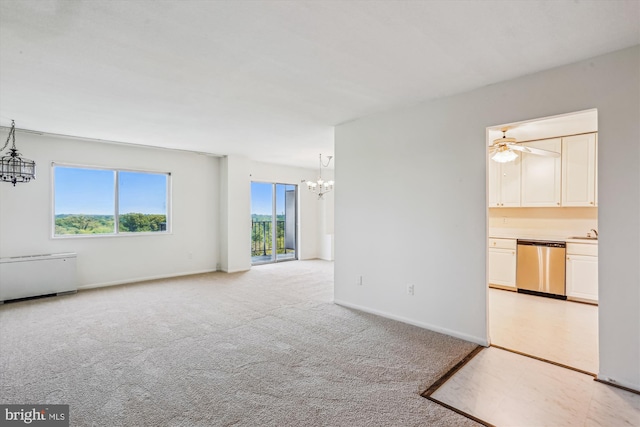 unfurnished living room with a healthy amount of sunlight, baseboards, light carpet, and ceiling fan with notable chandelier