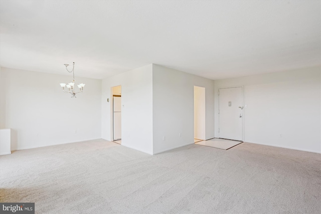 spare room featuring an inviting chandelier, baseboards, and light colored carpet