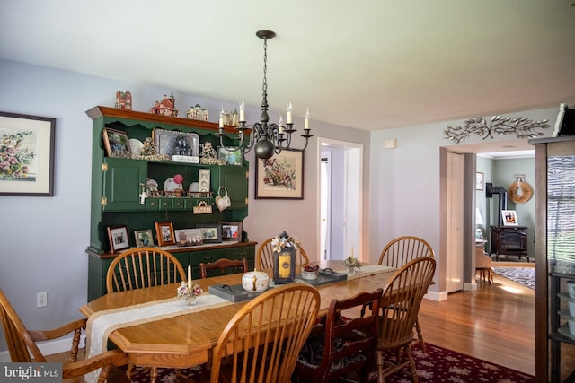 dining space with baseboards, a wood stove, wood finished floors, and a chandelier