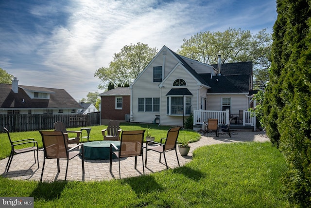 rear view of property featuring a fire pit, fence, a deck, a patio area, and a lawn