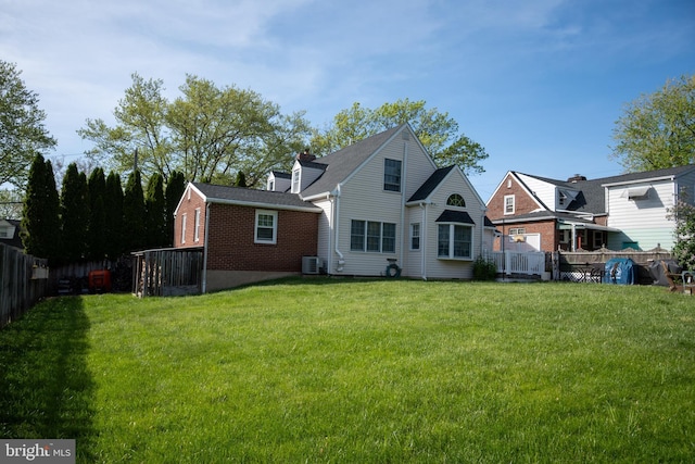 back of house featuring a fenced backyard, a yard, central AC, and brick siding