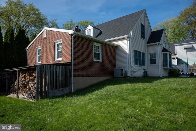 rear view of property with a lawn, a chimney, brick siding, and cooling unit