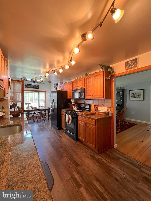 kitchen with dark wood-type flooring, a sink, decorative backsplash, and black appliances