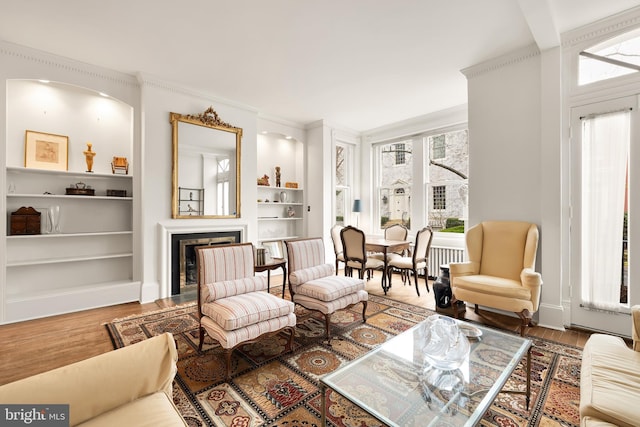 living area featuring crown molding, built in shelves, wood finished floors, and a fireplace