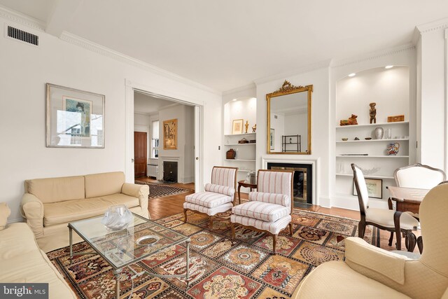 living room with crown molding, visible vents, built in features, wood finished floors, and baseboards