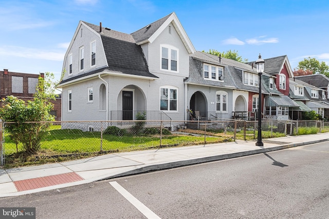 view of front facade featuring brick siding, a fenced front yard, roof with shingles, and a residential view