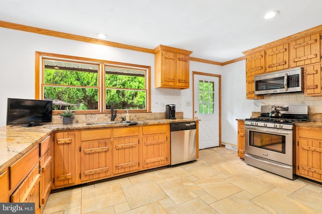 kitchen with appliances with stainless steel finishes, a sink, backsplash, crown molding, and light stone countertops