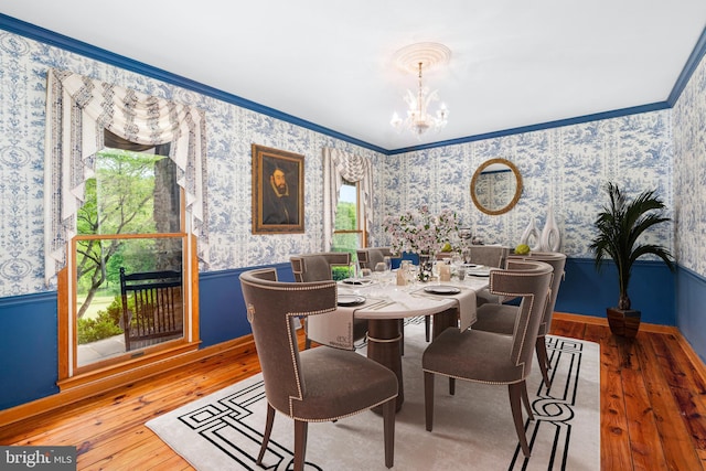 dining area featuring wallpapered walls, hardwood / wood-style flooring, a chandelier, ornamental molding, and healthy amount of natural light