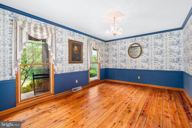 empty room with a chandelier, wallpapered walls, hardwood / wood-style flooring, plenty of natural light, and wainscoting