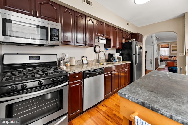 kitchen featuring visible vents, light wood-style floors, arched walkways, a sink, and stainless steel appliances