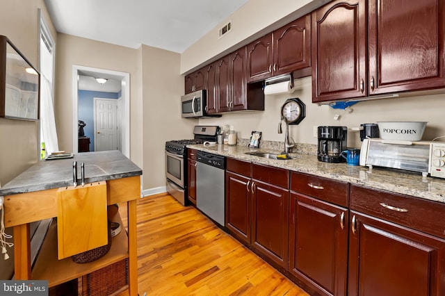 kitchen with light stone countertops, a sink, stainless steel appliances, light wood-type flooring, and visible vents