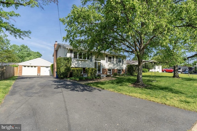 bi-level home featuring a front lawn, fence, an outbuilding, and a detached garage