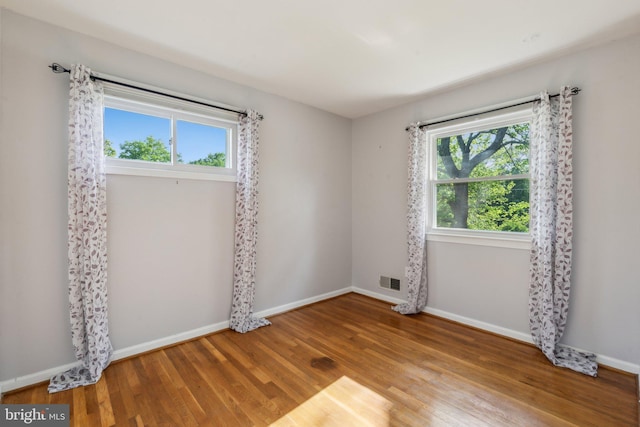 spare room featuring baseboards, visible vents, wood finished floors, and a wealth of natural light