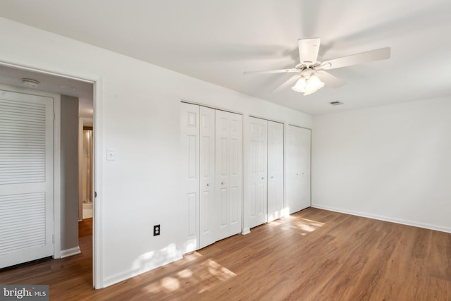 unfurnished bedroom with two closets, baseboards, ceiling fan, and wood finished floors