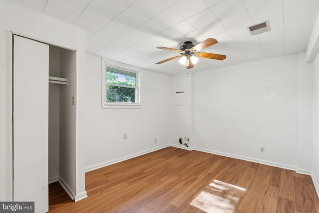 unfurnished bedroom featuring a ceiling fan, visible vents, wood finished floors, baseboards, and a closet