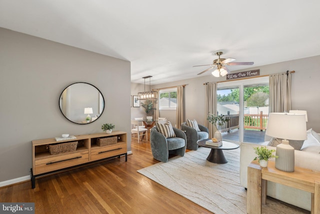 living area featuring baseboards, wood finished floors, and ceiling fan with notable chandelier