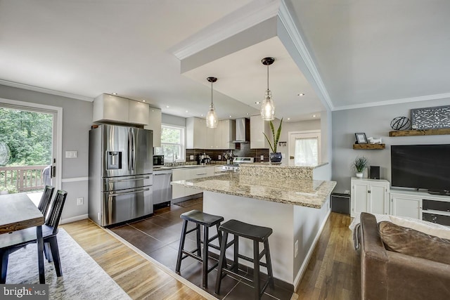 kitchen with stainless steel appliances, wall chimney exhaust hood, dark wood-style flooring, a breakfast bar, and crown molding