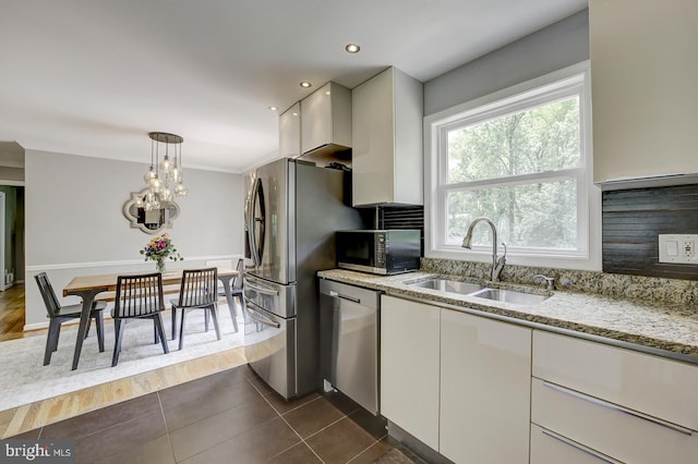 kitchen featuring stainless steel appliances, a sink, white cabinets, light stone counters, and hanging light fixtures