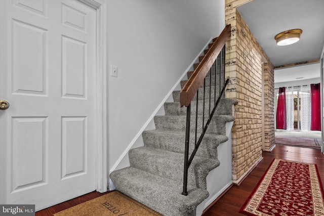 staircase with wood finished floors and brick wall