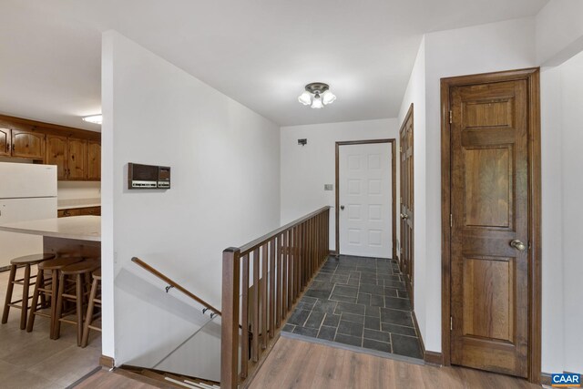 hallway with dark wood-type flooring, baseboards, and an upstairs landing