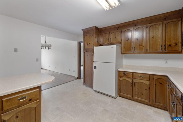 kitchen with brown cabinetry, freestanding refrigerator, light floors, light countertops, and a notable chandelier