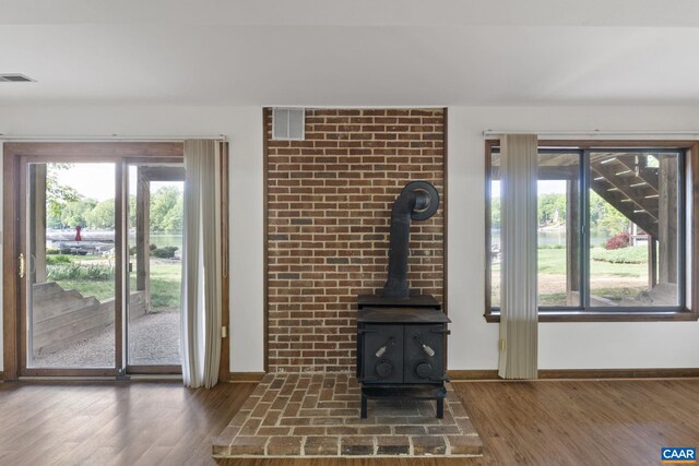 unfurnished living room featuring baseboards, a wood stove, wood finished floors, and visible vents