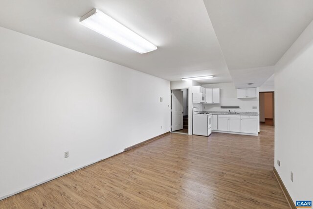 unfurnished living room with baseboards, a sink, and light wood-type flooring