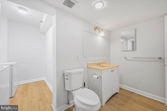 bathroom featuring visible vents, wood finished floors, baseboards, toilet, and separate washer and dryer