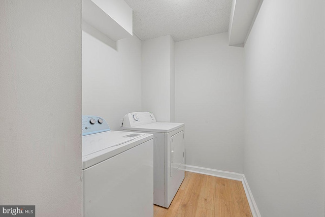 clothes washing area with laundry area, washer and dryer, baseboards, a textured ceiling, and light wood finished floors