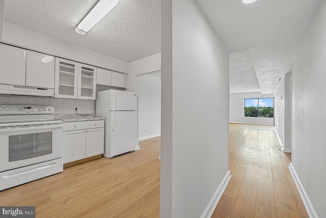 kitchen with light wood-type flooring, under cabinet range hood, white cabinets, and white appliances