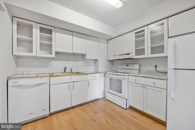 kitchen featuring a sink, light countertops, white cabinets, under cabinet range hood, and white appliances