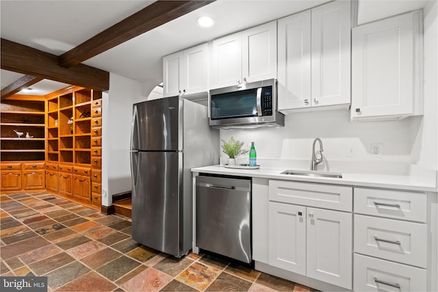 kitchen with stainless steel appliances, a sink, stone tile floors, beamed ceiling, and white cabinets