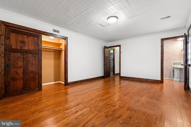 unfurnished bedroom with wood finished floors, ornamental molding, baseboards, and a closet