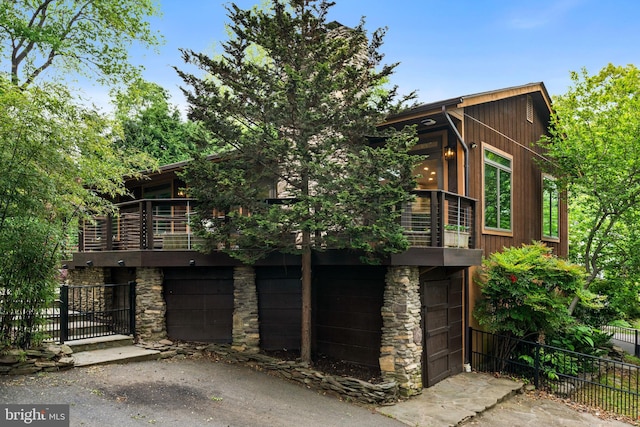 view of front of property with fence, a balcony, stone siding, and an attached garage