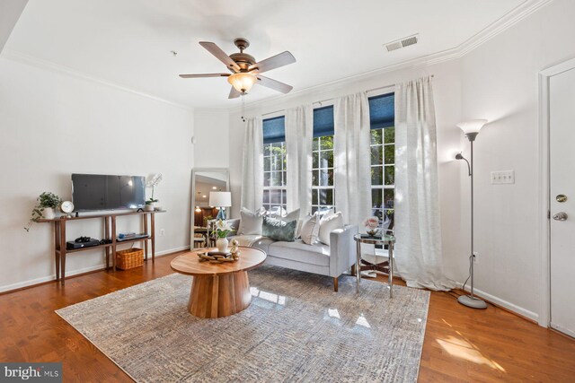 living room featuring a ceiling fan, visible vents, wood finished floors, baseboards, and ornamental molding