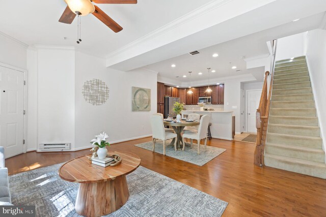 living area featuring crown molding, a ceiling fan, visible vents, stairway, and a baseboard radiator