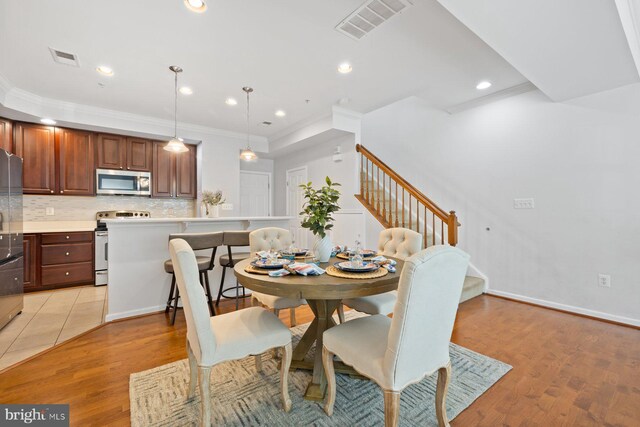 dining area featuring visible vents, ornamental molding, light wood-style flooring, and stairway